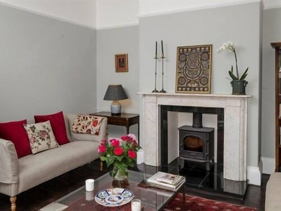 Una sala de estar con un sofá, una chimenea, una mesa con un florero y una lámpara.