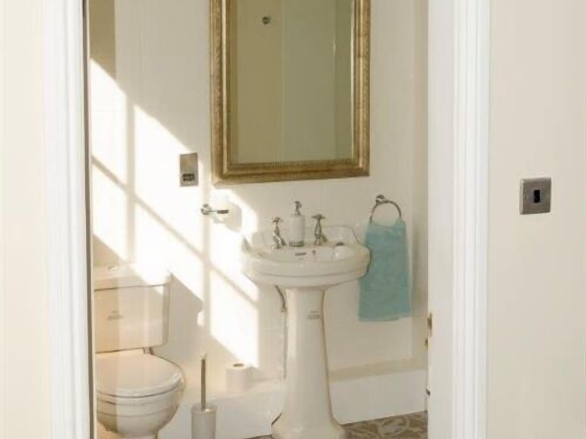 Une salle de bain avec un lavabo sur colonne, des toilettes et un miroir au-dessus du lavabo.