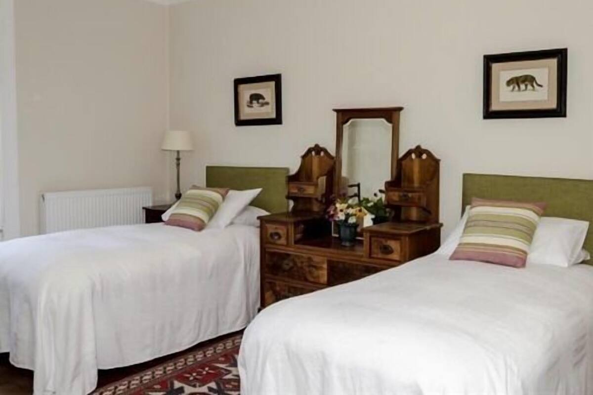 Quarto de hotel com duas camas de solteiro, penteadeira de madeira, espelho e quadros nas paredes.