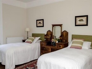 A hotel room with two single beds, a wooden dresser, a mirror, and framed pictures on the wall. - The Lions (Newark)