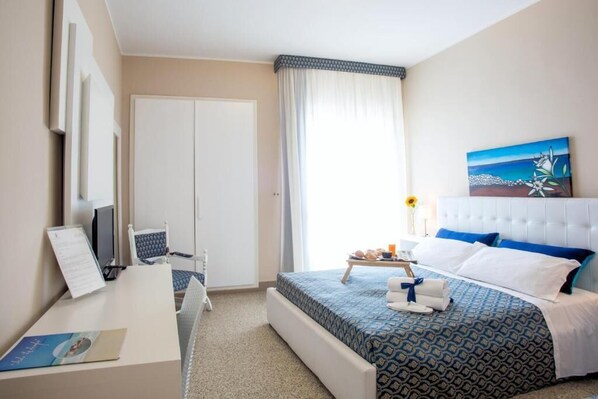 Una habitación de hotel con cama, escritorio, silla, televisión y un cuadro en la pared.