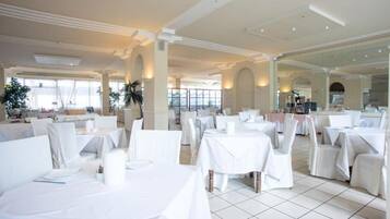 A spacious dining area with white tables and chairs, large windows, and a modern architectural design.