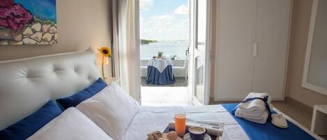 A hotel room with a bed, breakfast tray, and a view of the sea.
