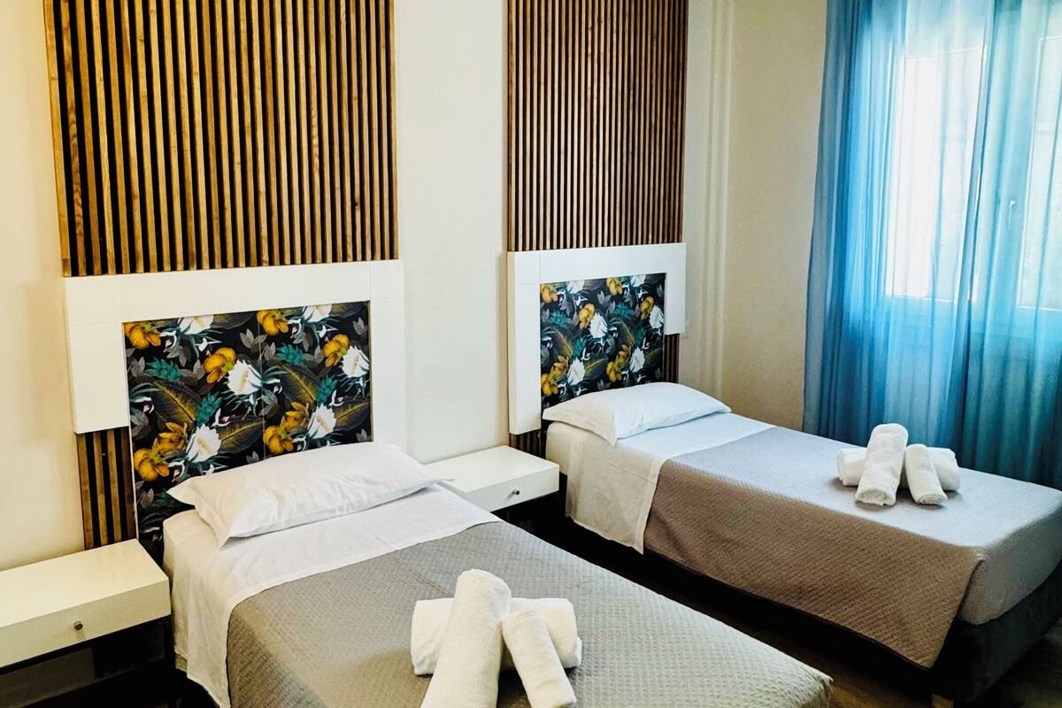 Habitació d'hotel amb dos llits, panells de fusta a les parets, una finestra amb cortines blaves i un sòl de fusta.