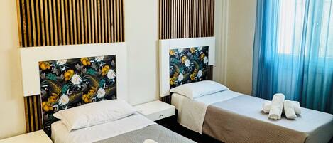 A hotel room with two beds, wooden paneling on the walls, a window with blue curtains, and a wooden floor.