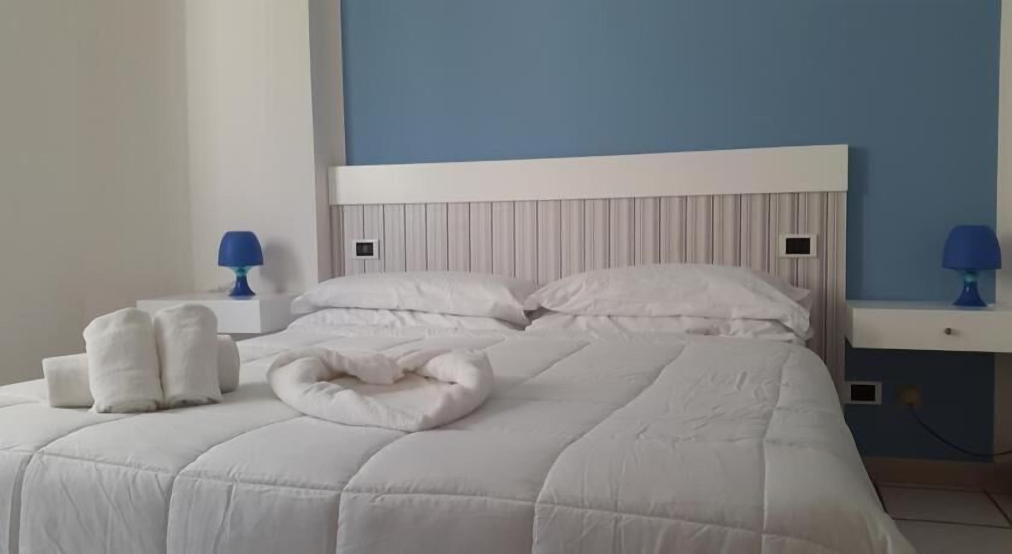 Un letto rifatto con biancheria e cuscini bianchi, una parete blu e due comodini con lampade.