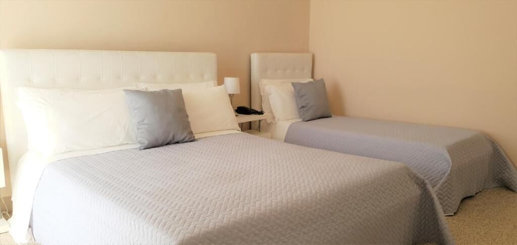 A hotel room with two beds, each with a headboard and pillows.