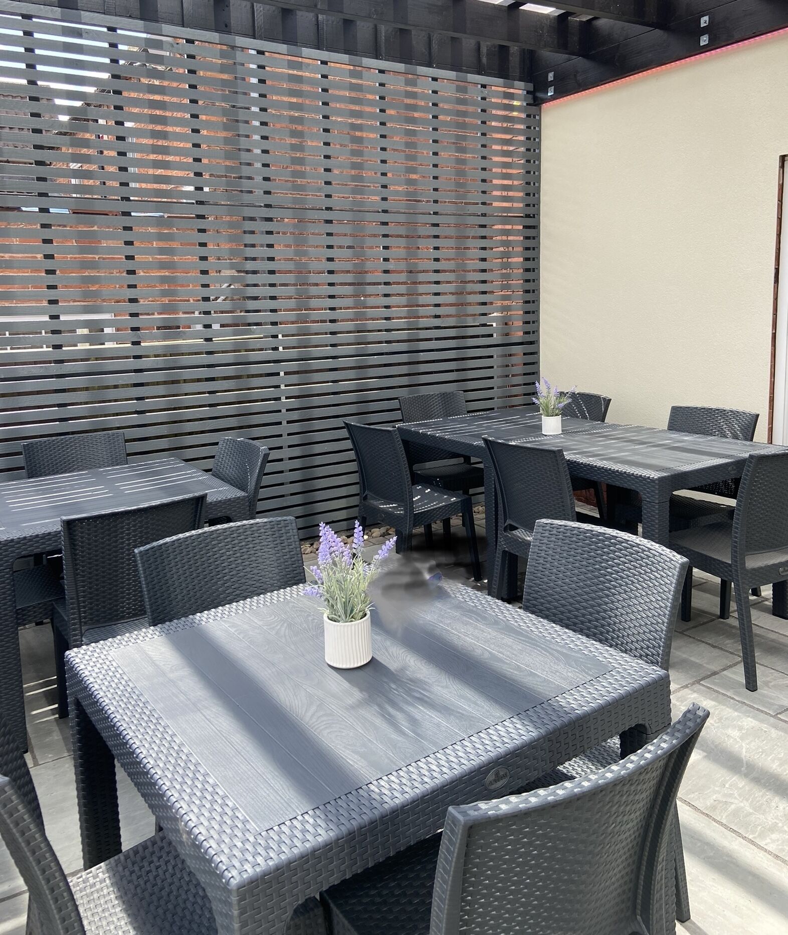 Un espace extérieur aménagé en terrasse, avec plusieurs tables et chaises, un mur décoratif et un pot de fleurs.