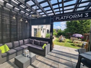 A covered outdoor seating area with a sofa and tables, a sign reading "PLATFORM 3 AT THE STATION HOTEL", and a view of the hotel entrance and garden. - The Station Hotel (Worksop)