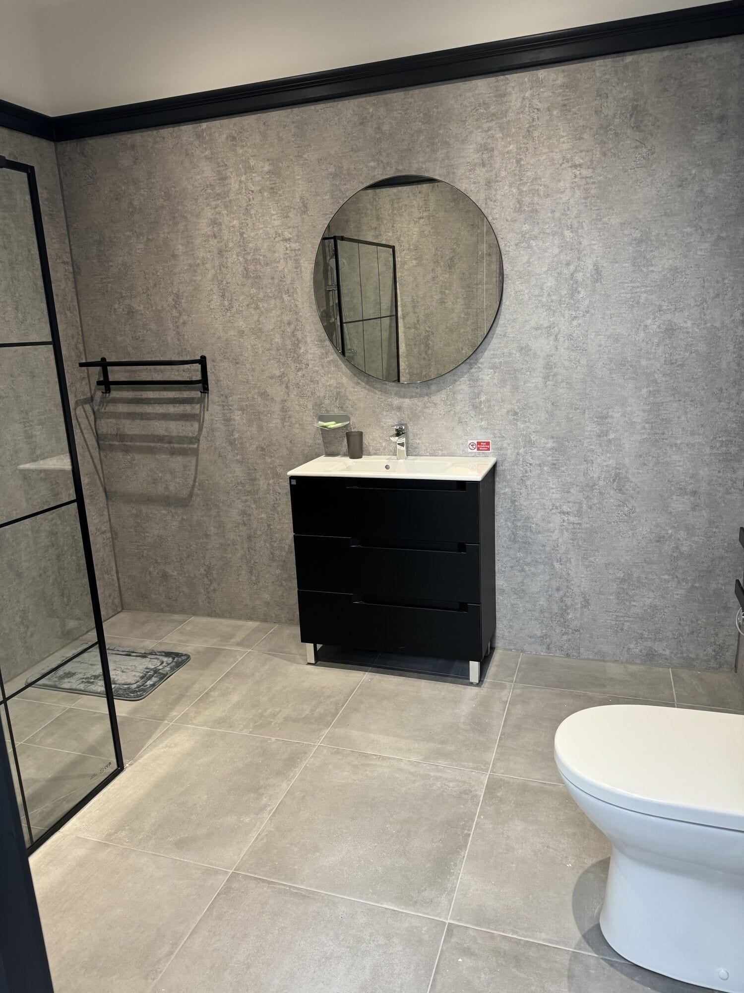 Een badkamer met een wit toilet, een zwart wastafelmeubel met een spiegel en een douchegedeelte.
