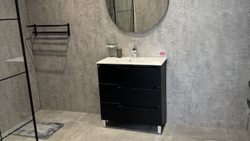 Un baño con inodoro blanco, tocador negro con espejo y zona de ducha.