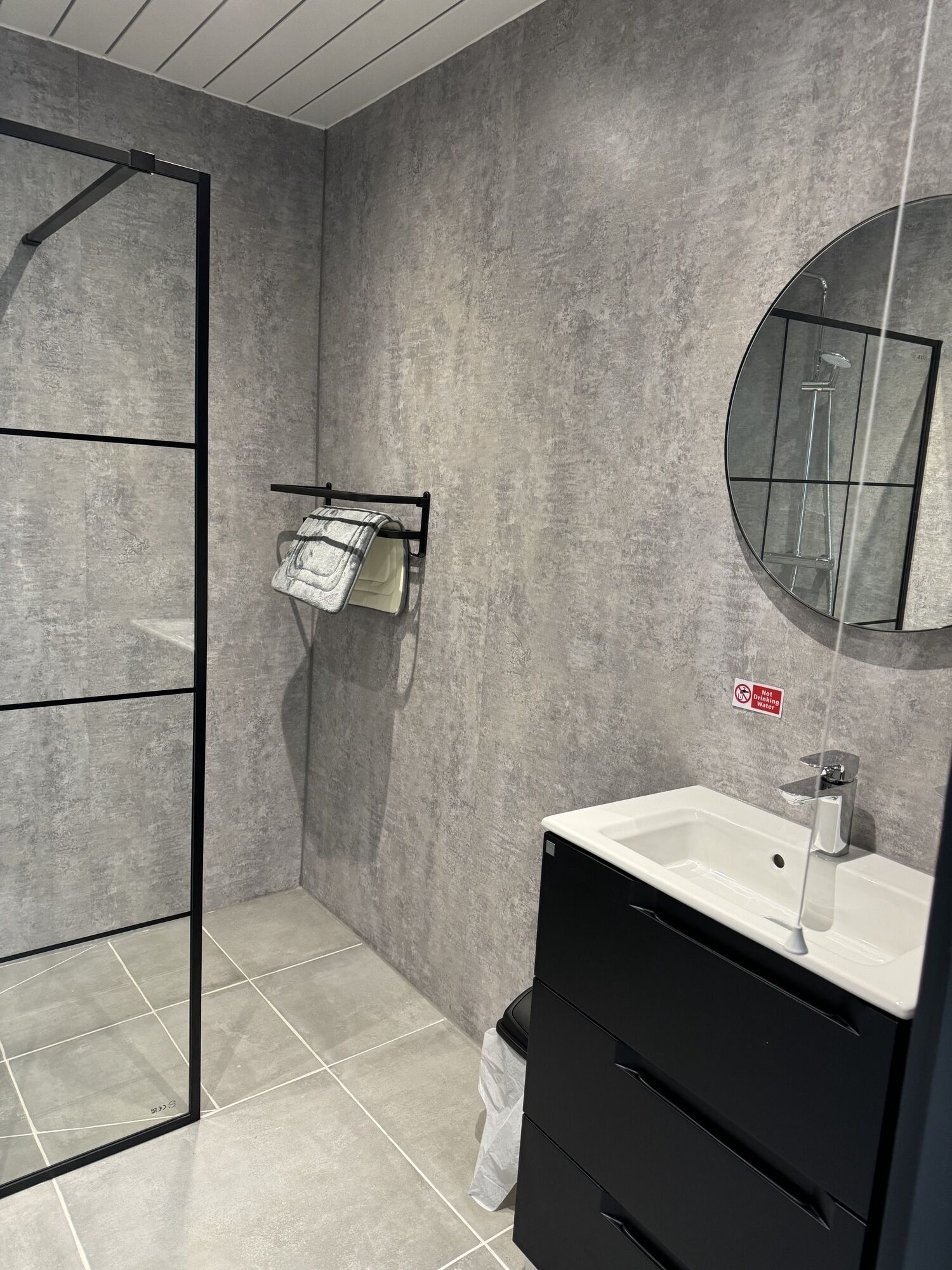 A modern bathroom with a shower, a sink, a mirror, and a towel rack.