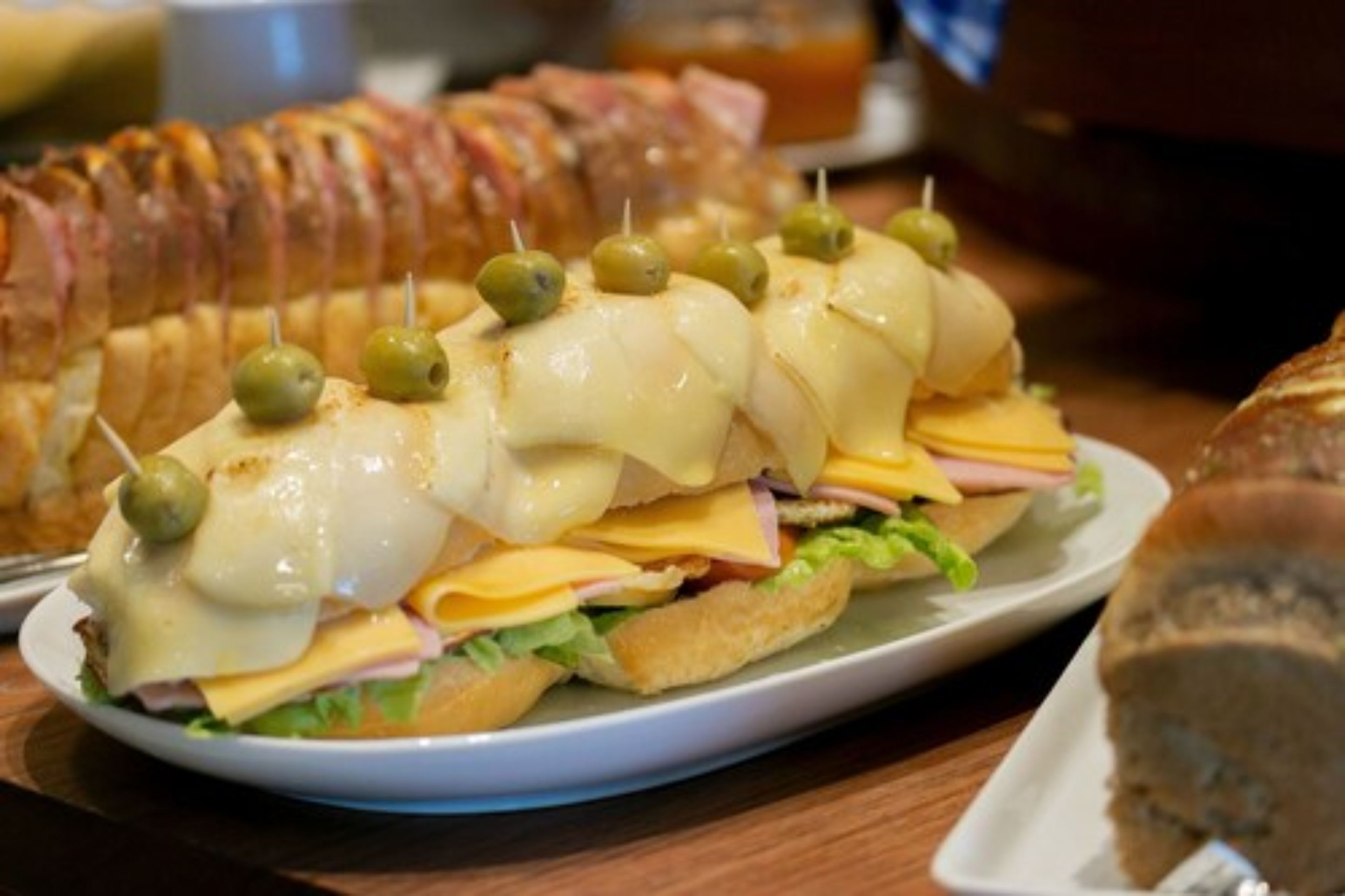 A sandwich with cheese, ham, and lettuce, garnished with olives, on a white plate.