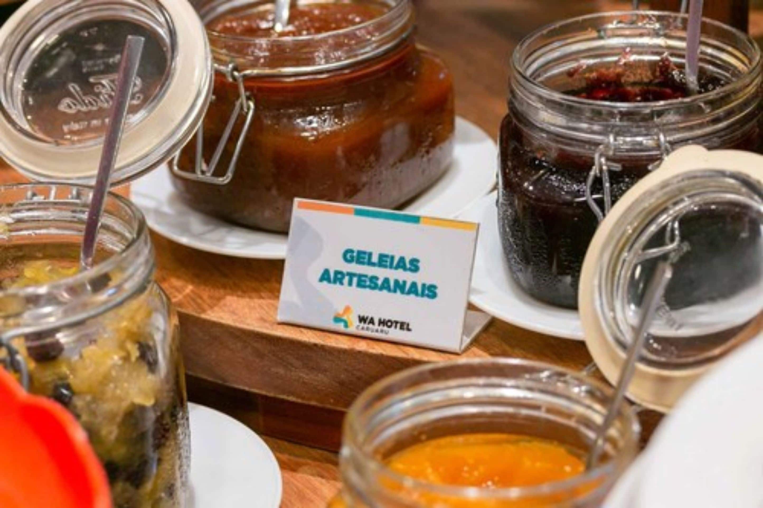 Ein Buffet mit verschiedenen Lebensmitteln in Gläsern, ein Schild mit der Aufschrift 'Geleias Artesanais' und das Logo des WA Hotels.