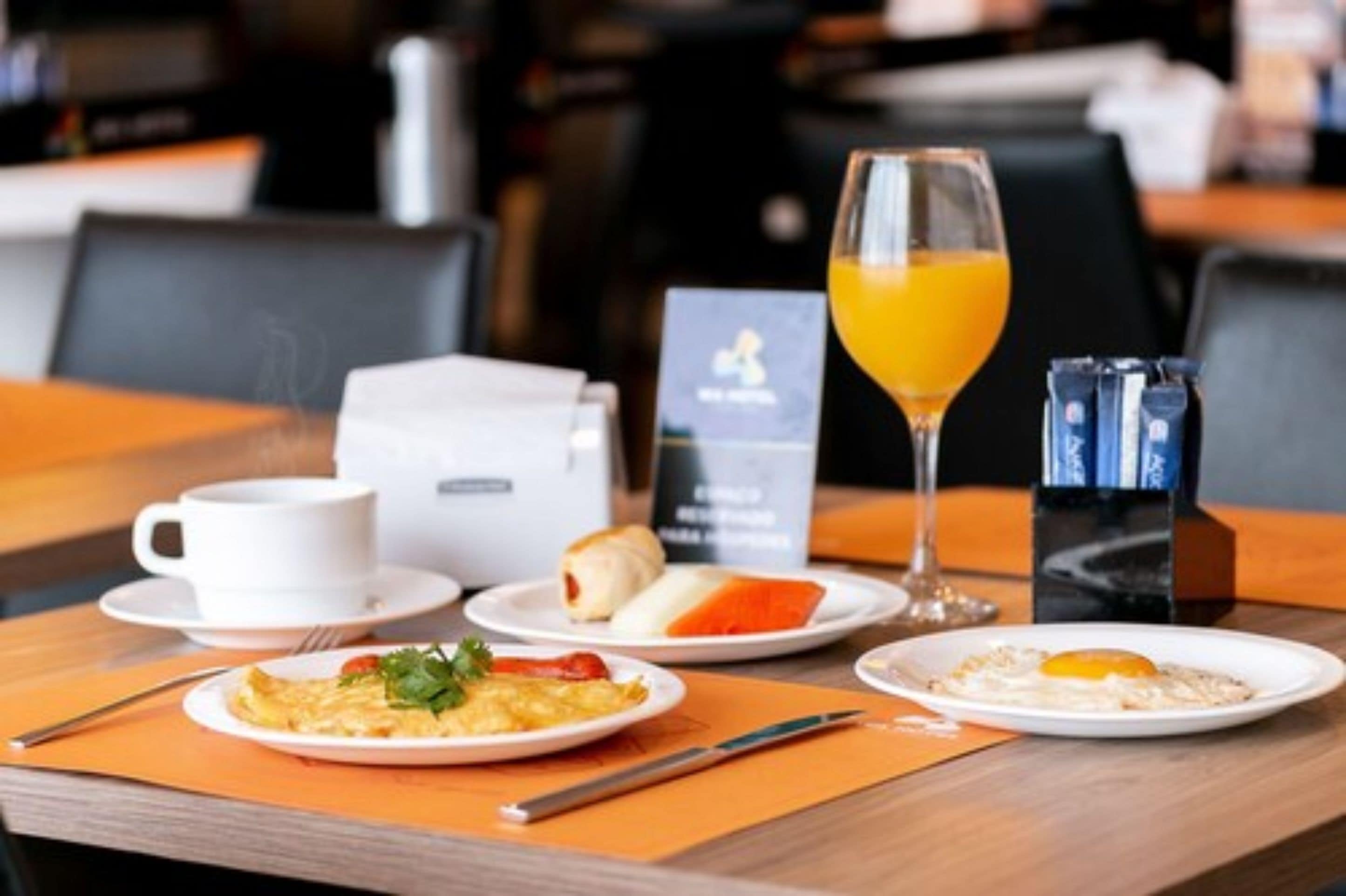 Desayuno con una taza de café, un vaso de jugo de naranja y platos de comida que incluyen huevos y pasteles.