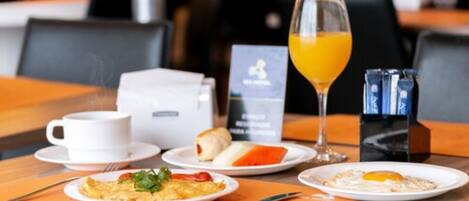 Desayuno con una taza de café, un vaso de jugo de naranja y platos de comida que incluyen huevos y pasteles.