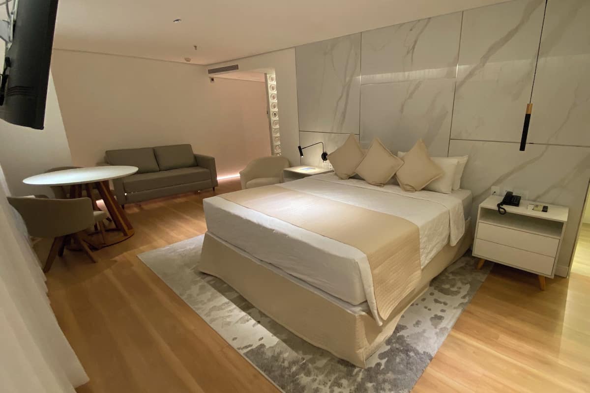 A modern bedroom with a large bed, a bedside table, a nightstand, a sofa, and a small round table.