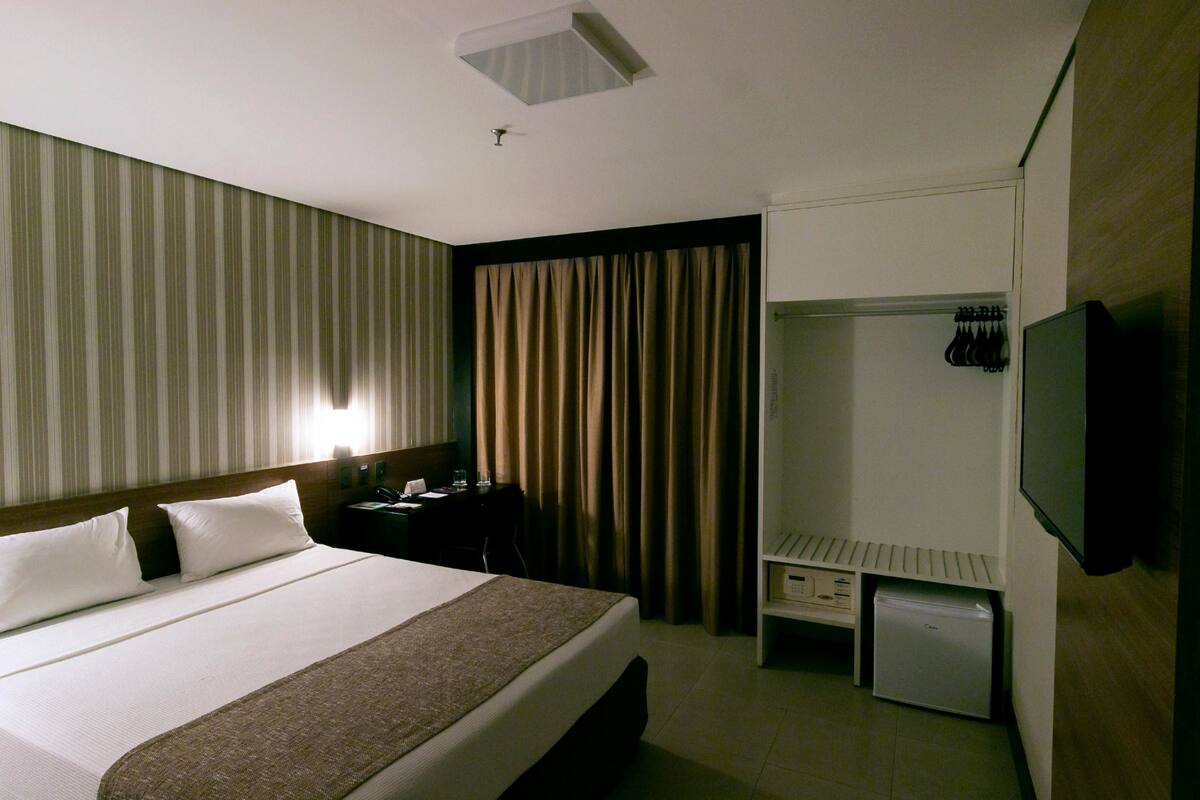 A hotel room with a bed, a desk, a wardrobe, and a television.