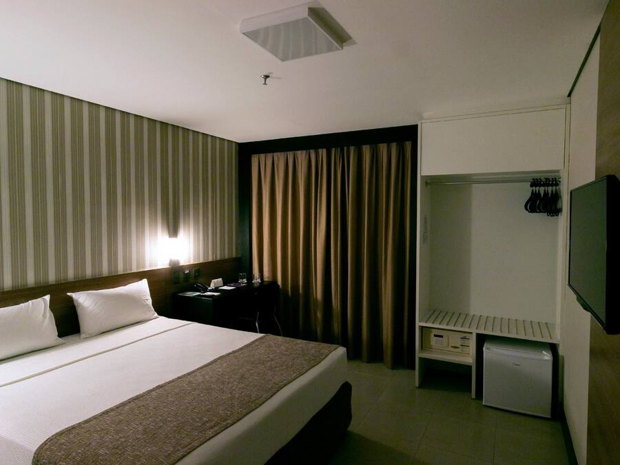 A hotel room with a bed, a desk, a wardrobe, and a television.