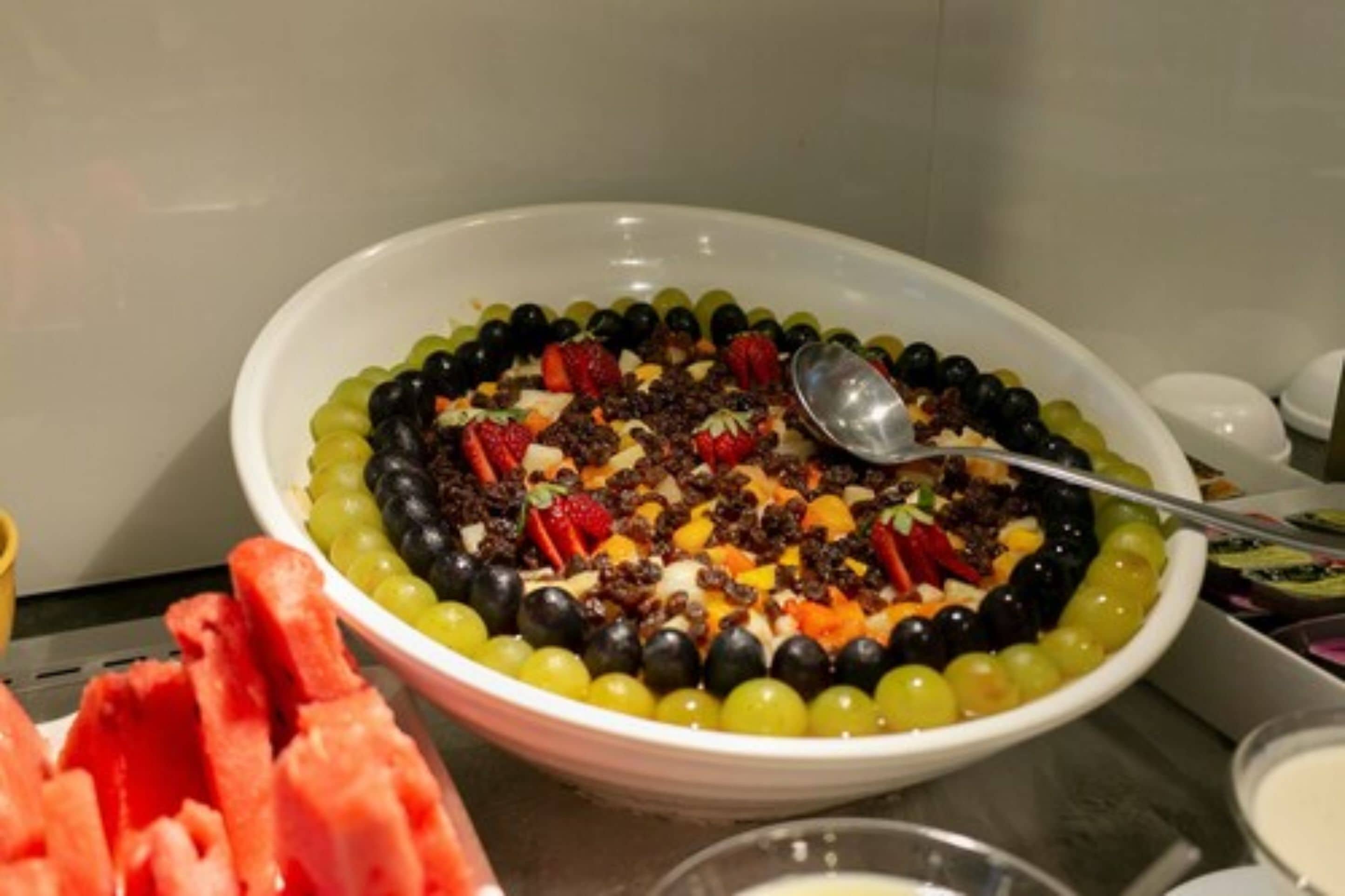 A bowl of fruit salad with a spoon, surrounded by watermelon slices.