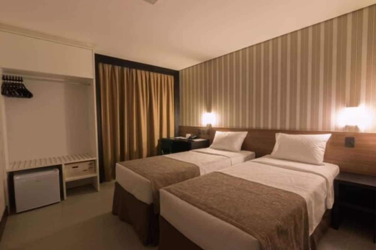 A hotel room with two beds, a wardrobe, a desk, and a nightstand.