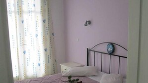 A bedroom with a bed, a bedside table, a lamp, and a window with curtains. - Very-Kokkos Pension 2 (Naxos)
