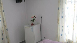 A bedroom with a bed, a small white cabinet, a television, and an air conditioner. - Very-Kokkos Pension 2 (Naxos)