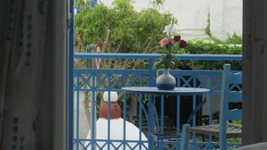 A room with a bed, a blue balcony railing, and a view of a white building with a red roof. - Very-Kokkos Pension 2 (Naxos)