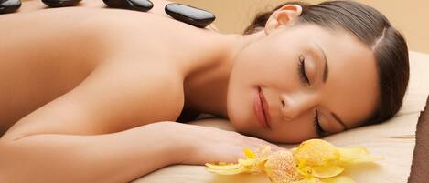 A person lying on a massage table with stones and a flower.