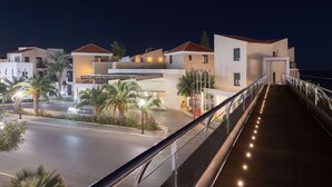 A modern hotel with a covered walkway, palm trees, and a view of the sea. - Iolida Beach by Smile Hotels (Chania)