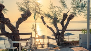 A terrace with a view of the sea at sunset, featuring a table and chairs, a hammock, and a wooden fence. - Iolida Beach by Smile Hotels (Chania)