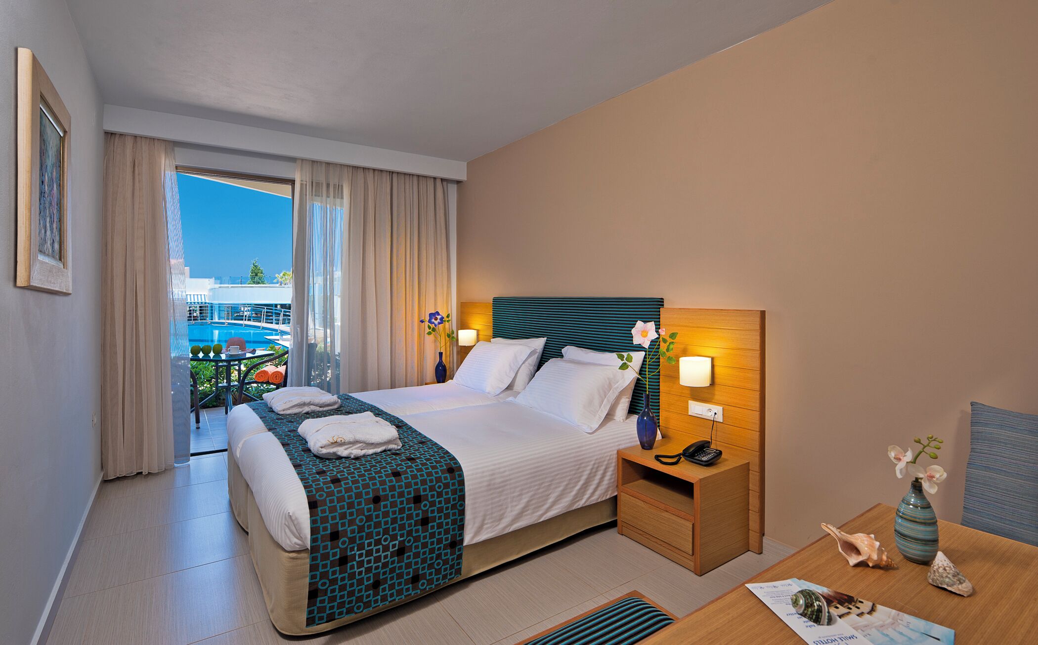 Habitación de hotel con cama, mesita de noche con lámpara, vista a la piscina y balcón.
