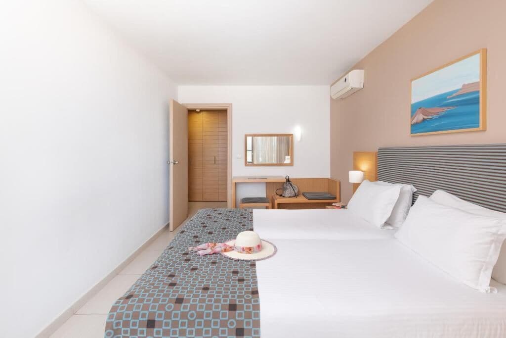 Una habitación de hotel con cama, escritorio, silla, lámpara y un cuadro en la pared.