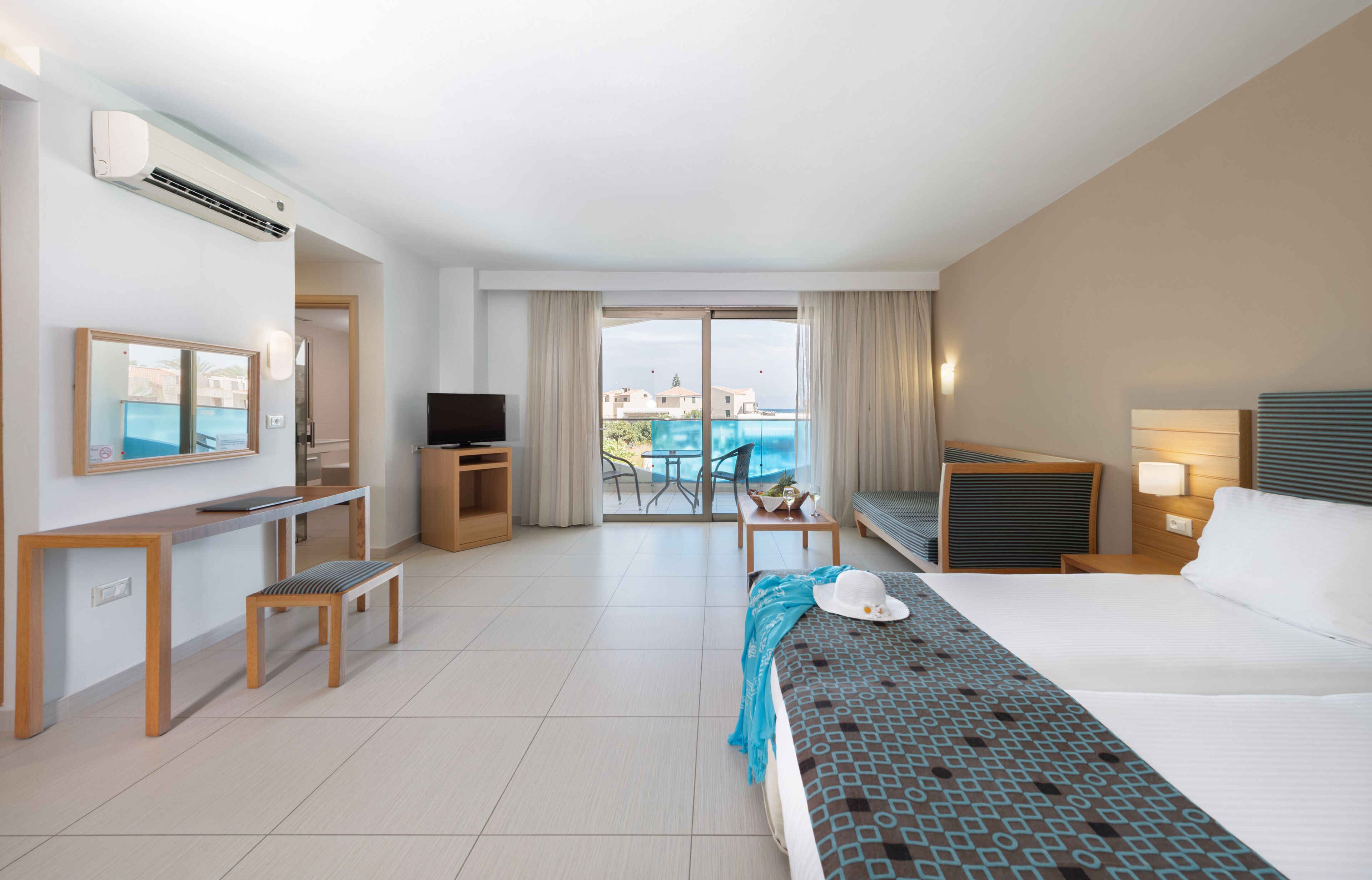 Habitación de hotel con cama, televisión, escritorio, silla, mesita y vista a la piscina.