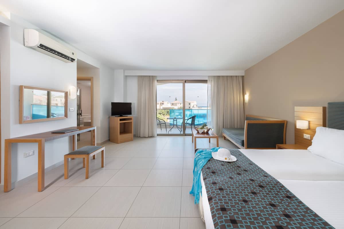 Habitación de hotel con cama, televisión, escritorio, silla, mesita y vista a la piscina.