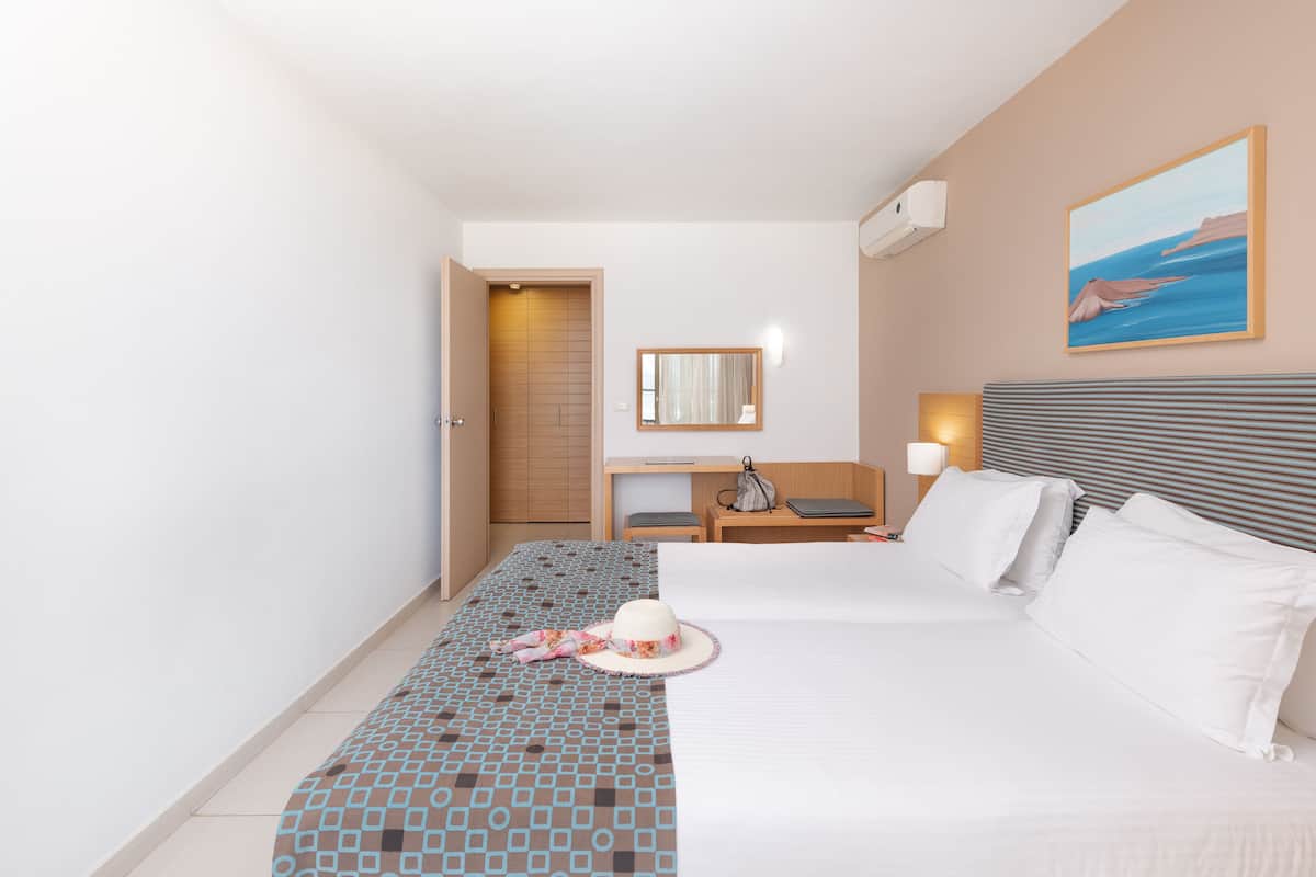 A hotel room with a bed, a desk, a chair, a lamp, and a painting on the wall.