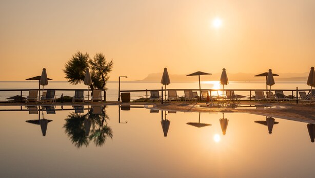A serene poolside area with lounge chairs and umbrellas, reflecting the sunset over the water. - Iolida Beach by Smile Hotels (Chania)