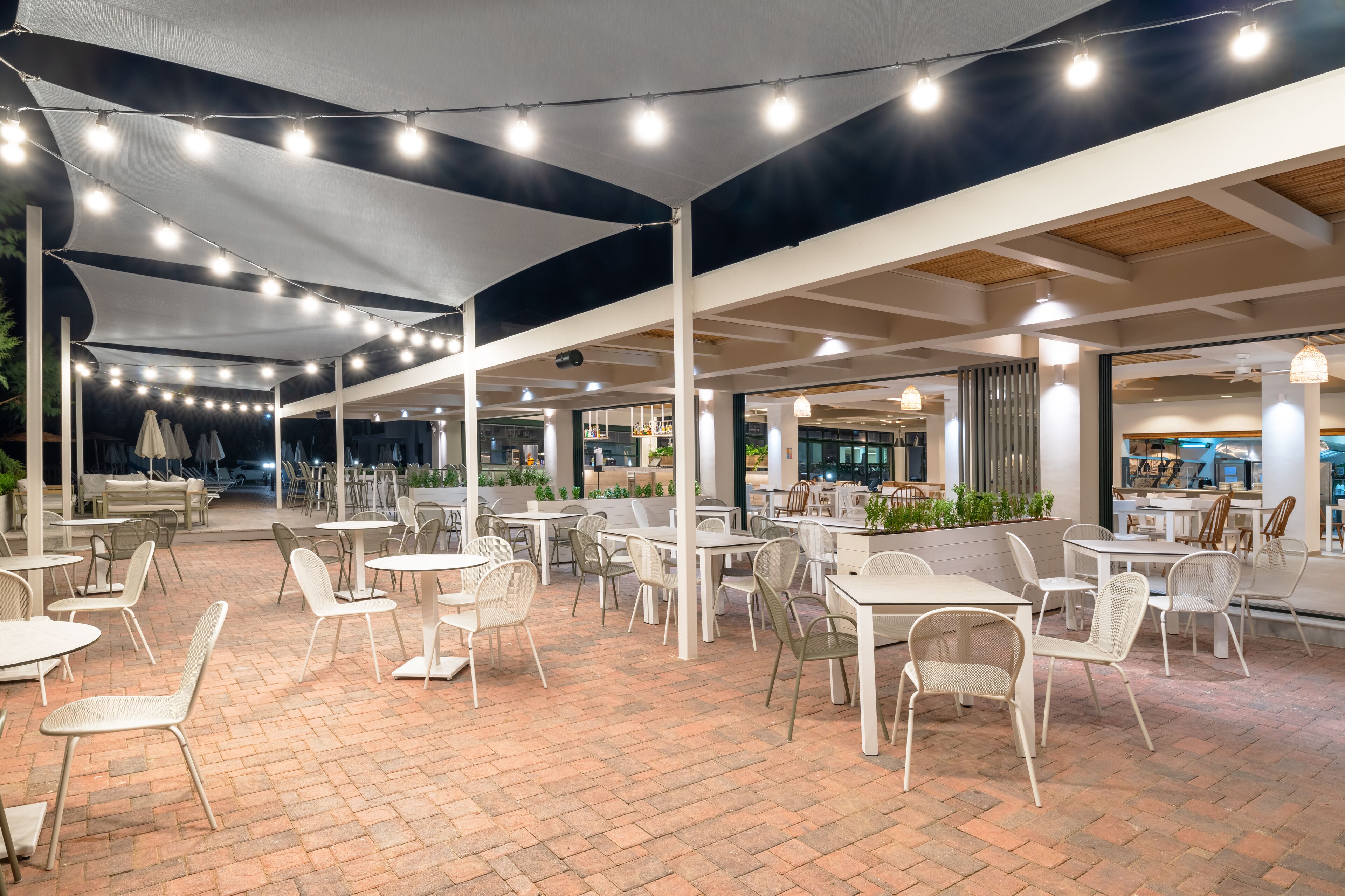 An outdoor cafe area with tables and chairs, covered by a canopy, and string lights.