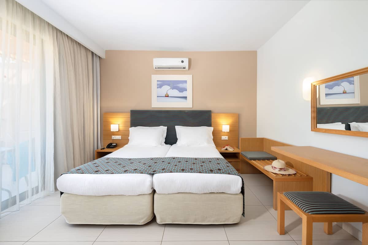 A hotel room with a large bed, two bedside tables, a desk, a chair, a mirror, and a window with curtains.