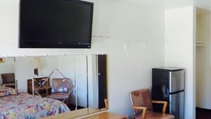 A hotel room with a bed, a chair, a television mounted on the wall, and a refrigerator. - Eagle Rock Motel (Los Angeles)