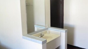 A bathroom with a white sink, a mirror, and a dark door. - Eagle Rock Motel (Los Angeles)