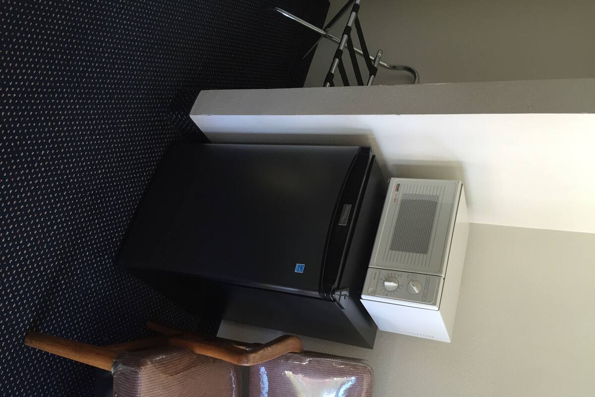 A room with a black printer, a white air conditioning unit, and a wooden chair with a plastic cover.