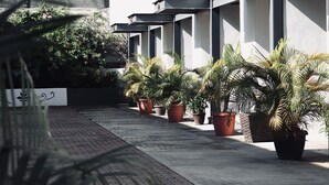 Un edificio moderno con un diseño geométrico y limpio, que cuenta con una serie de balcones y un camino pavimentado bordeado de plantas en macetas.