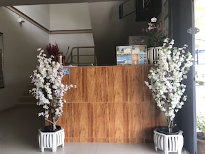 A reception desk with a wooden finish, two potted white flowering plants, and informational brochures on the counter. - B Place Guesthouse (Ko Phi Phi)