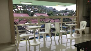 A balcony with white plastic chairs and a table, overlooking a residential area with houses and a pool. - B Place Guesthouse (Ko Phi Phi)