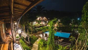 Estructura de madera con piscina y vegetación circundante de noche.