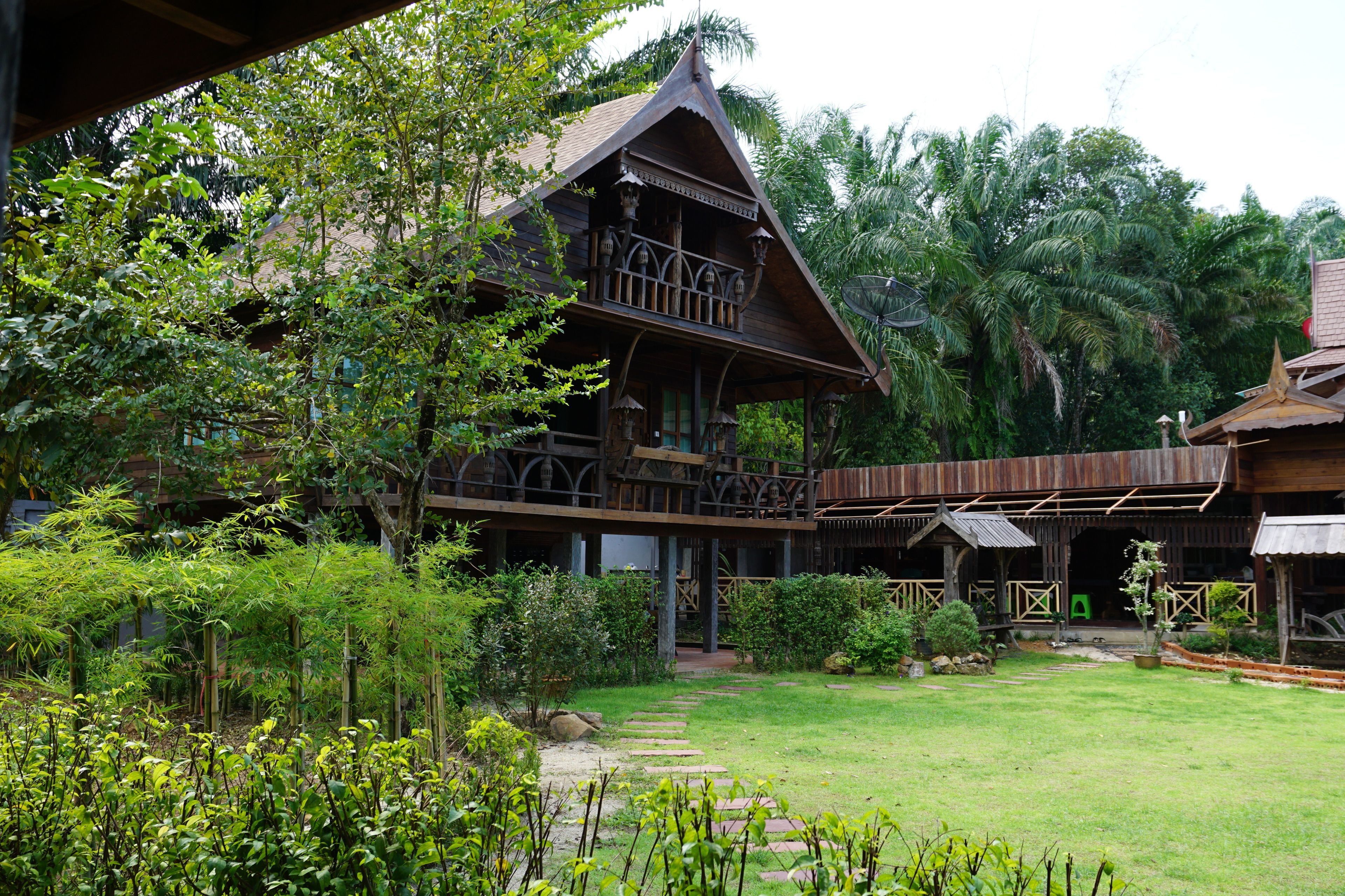 A traditional wooden house with a balcony, surrounded by lush greenery and a well-maintained garden.