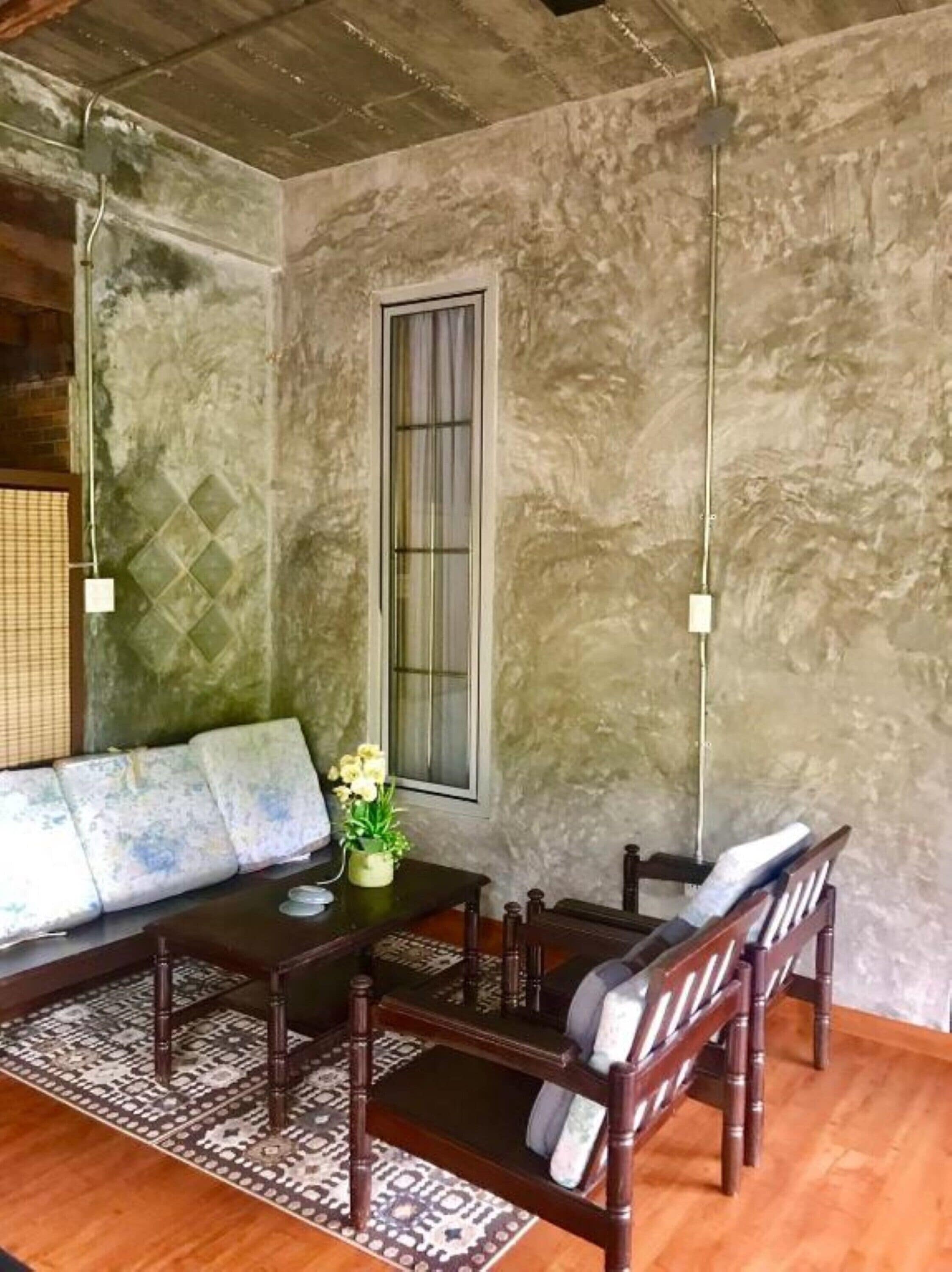 A room with a sofa, a table, and chairs. There is a window and a wall with a textured surface.
