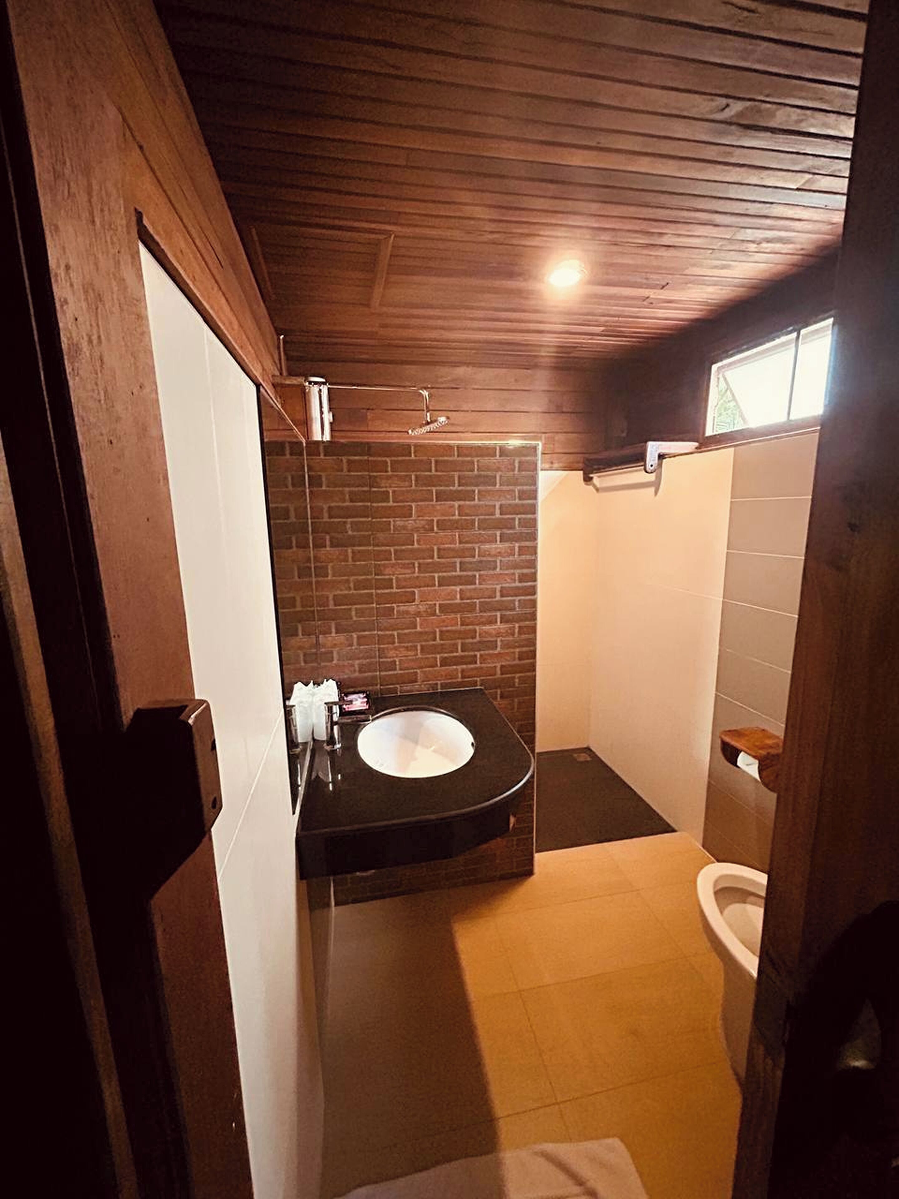 Un baño con un lavamanos negro, un inodoro blanco y una zona de ducha.