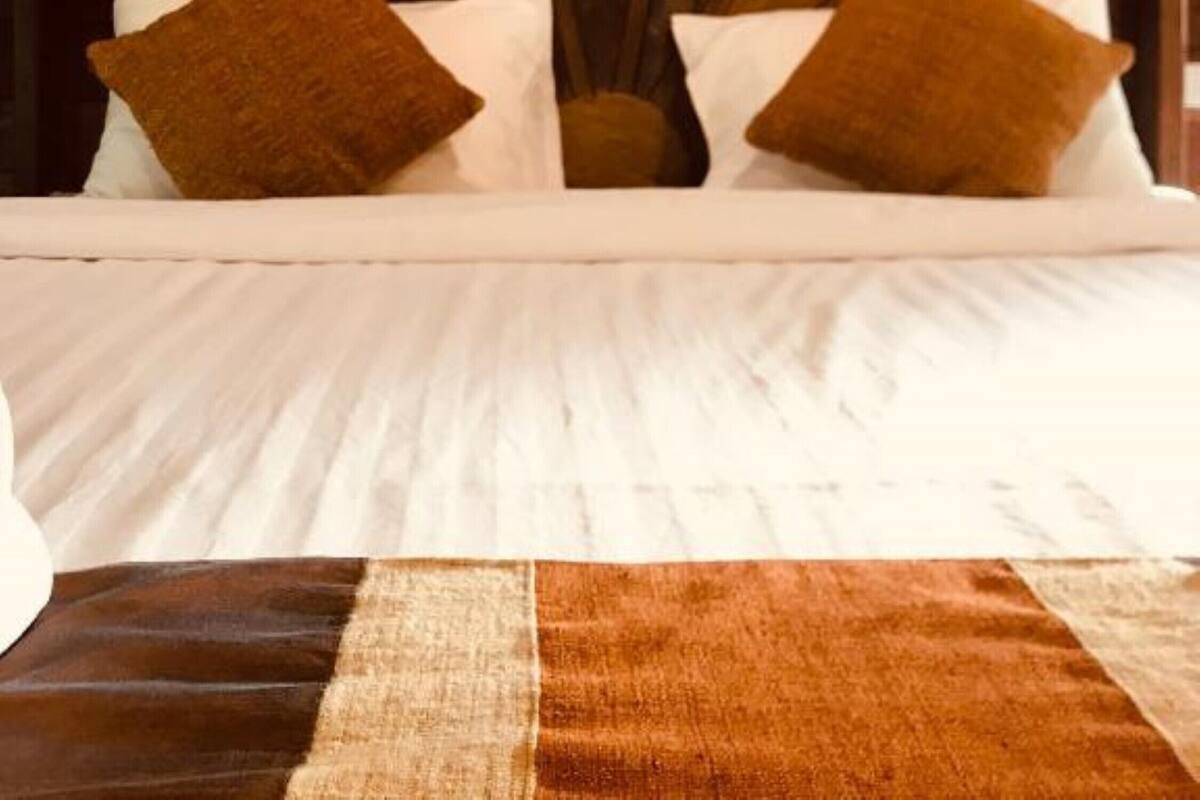 Ein Bett mit weißen Bettwäsche und braunen Kissen, vor einem Holzkopfende.